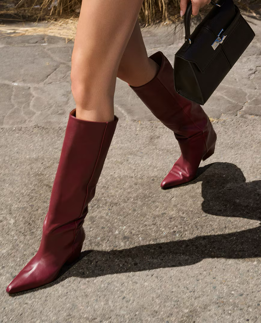 Person walking in red boots, holding a black handbag on a concrete path.