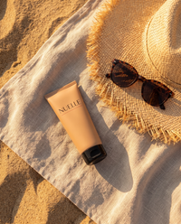 NUELLE Body Perfector tube on a linen beach towel with sun hat