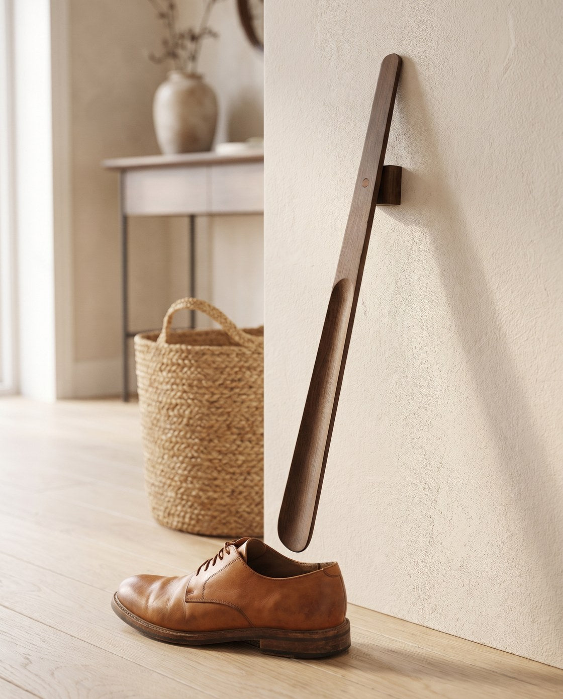 The Norlund magnetic shoehorn reaching down to a leather shoe on the floor by the front door of a warm Nordic entryway